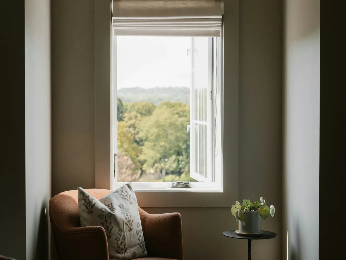 An armchair by an open window in the office, with trees outside