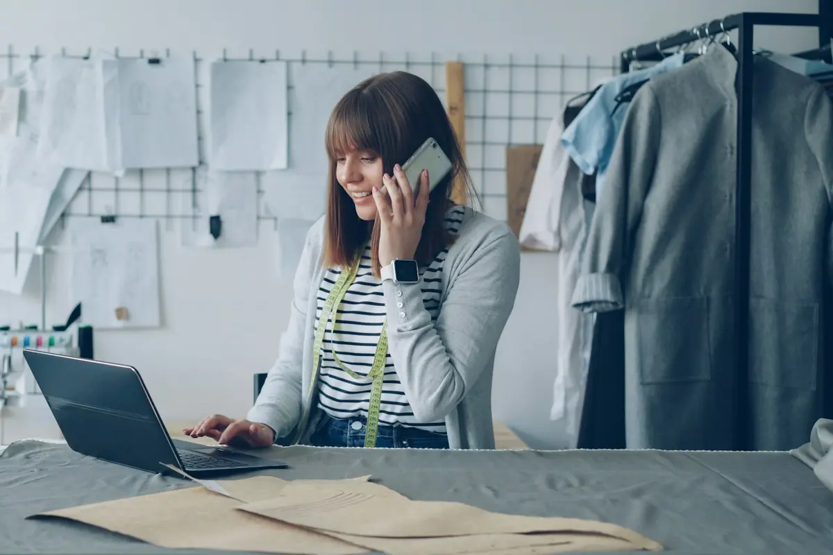 A designer on the phone at her studio workbench, laptop open