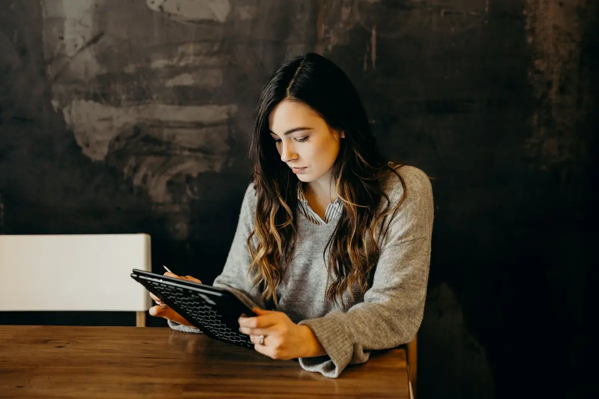 A woman at a wooden table looking closely at something on a tablet