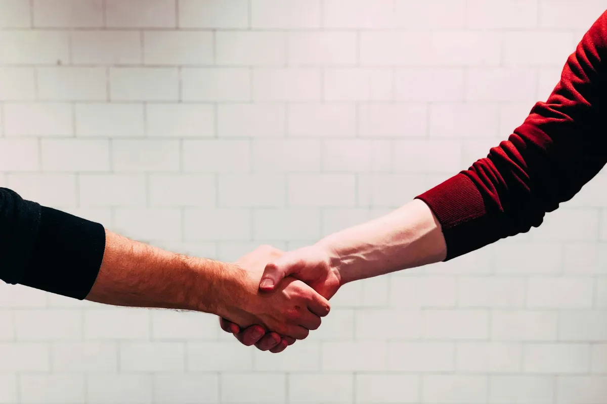 Two people shaking hands in front of a white brick wall