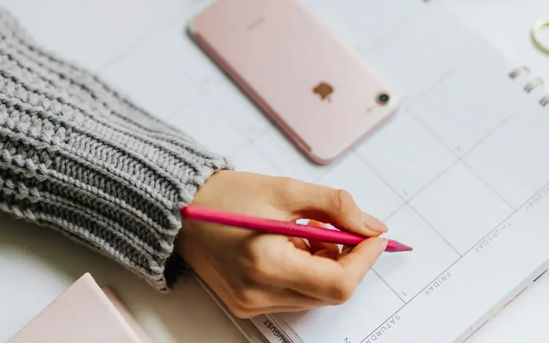 A hand writing in an appointment planner beside a phone