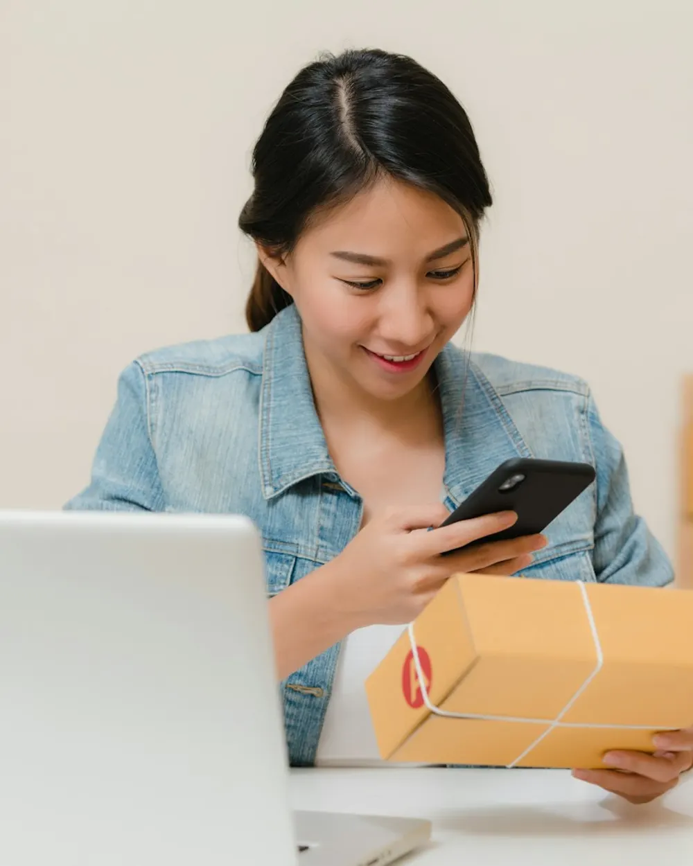 A small online shop owner checking an order on her phone beside a parcel