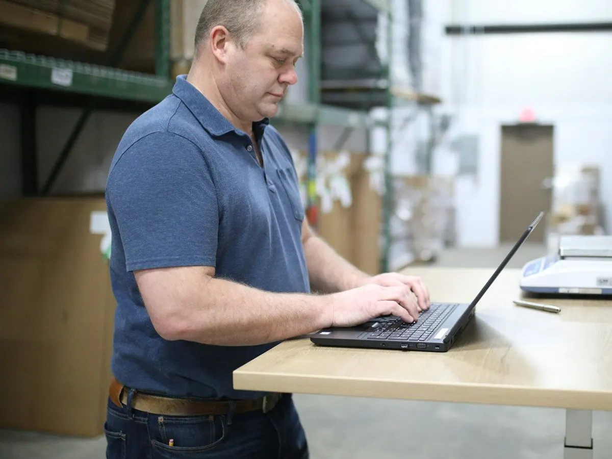 A warehouse owner working at a laptop on a standing desk