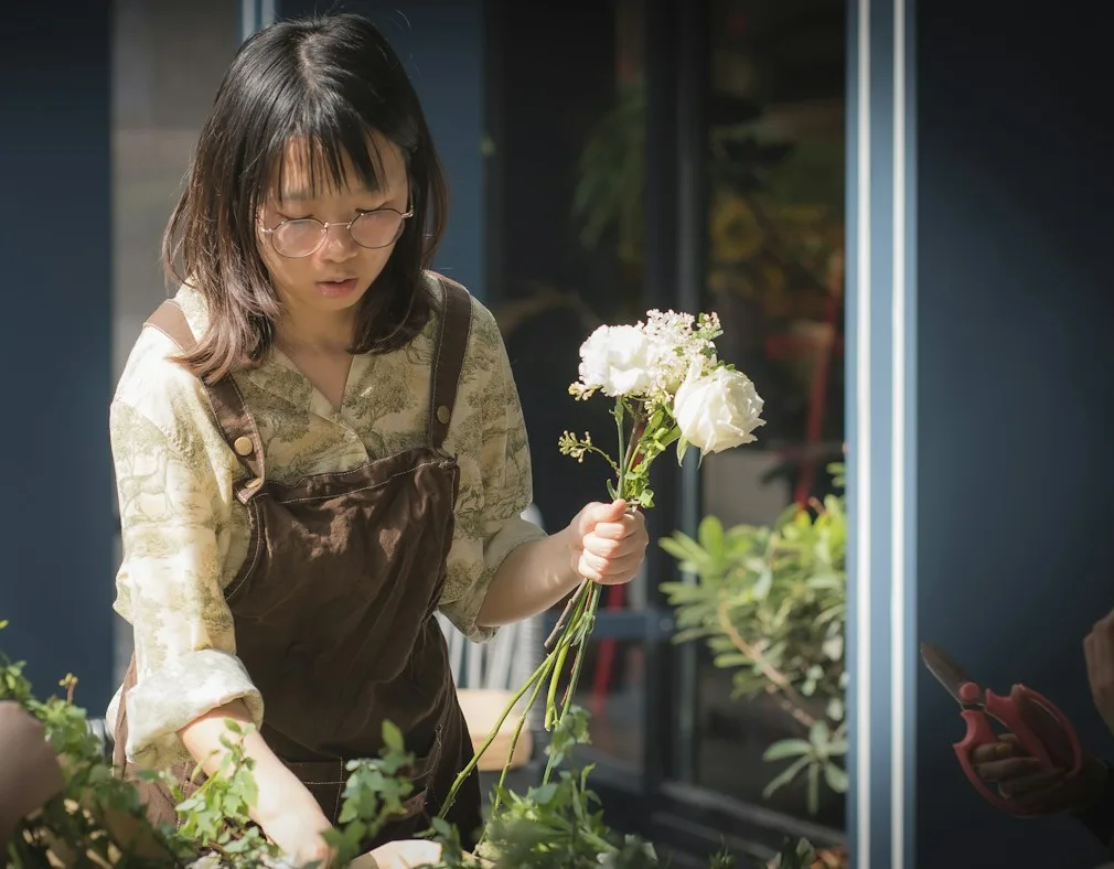 A florist in an apron arranging white flowers at her shop